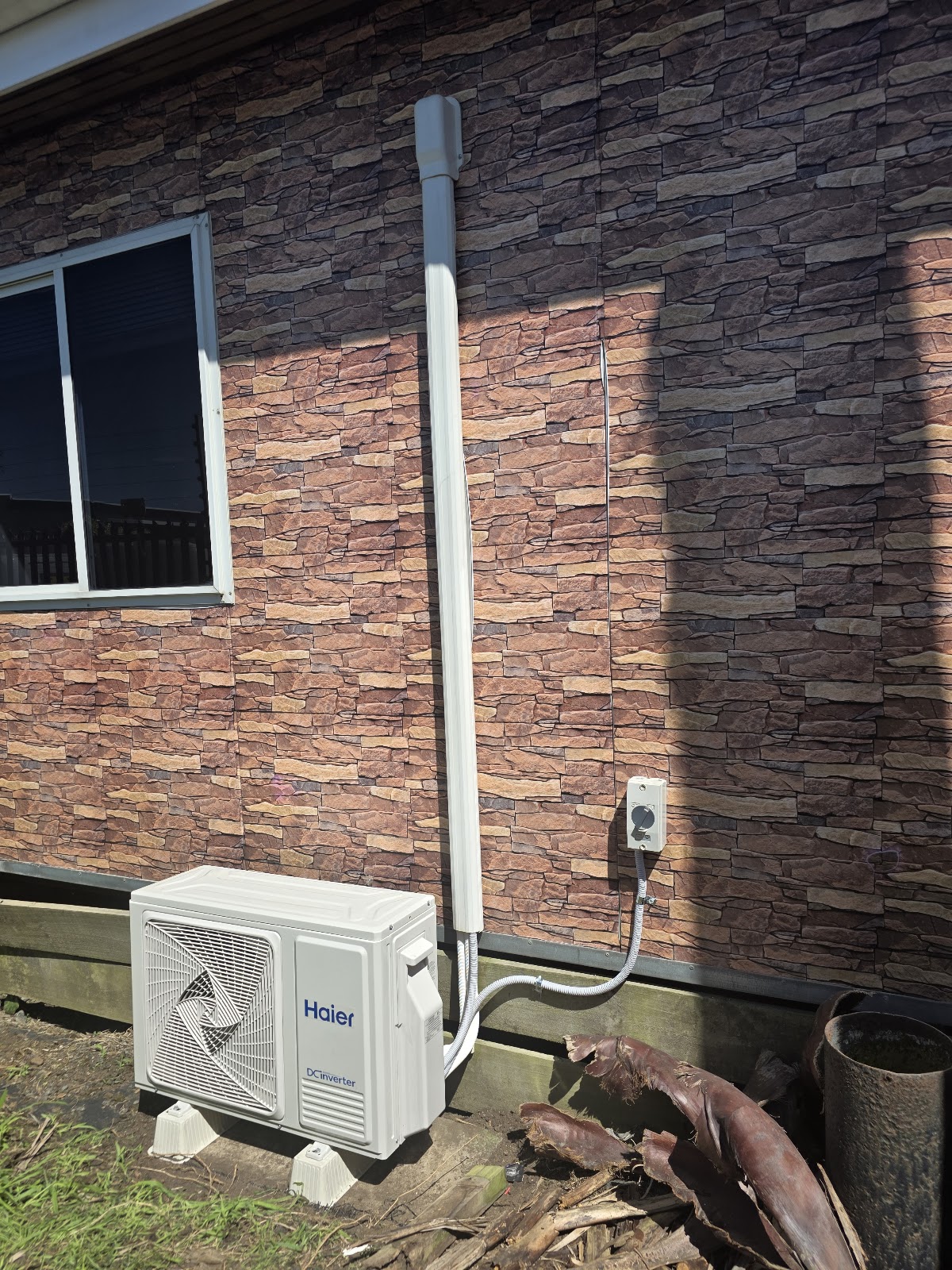 Haier heat pump outdoor unit installed against a stone clad wall